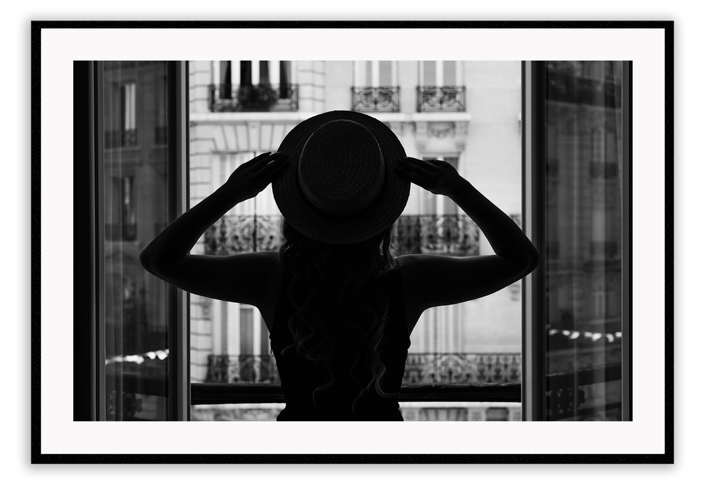 A vintage fashion wall art with a cinematic scene of a parisian woman wearing a hat looking out to the city on the balcony. 