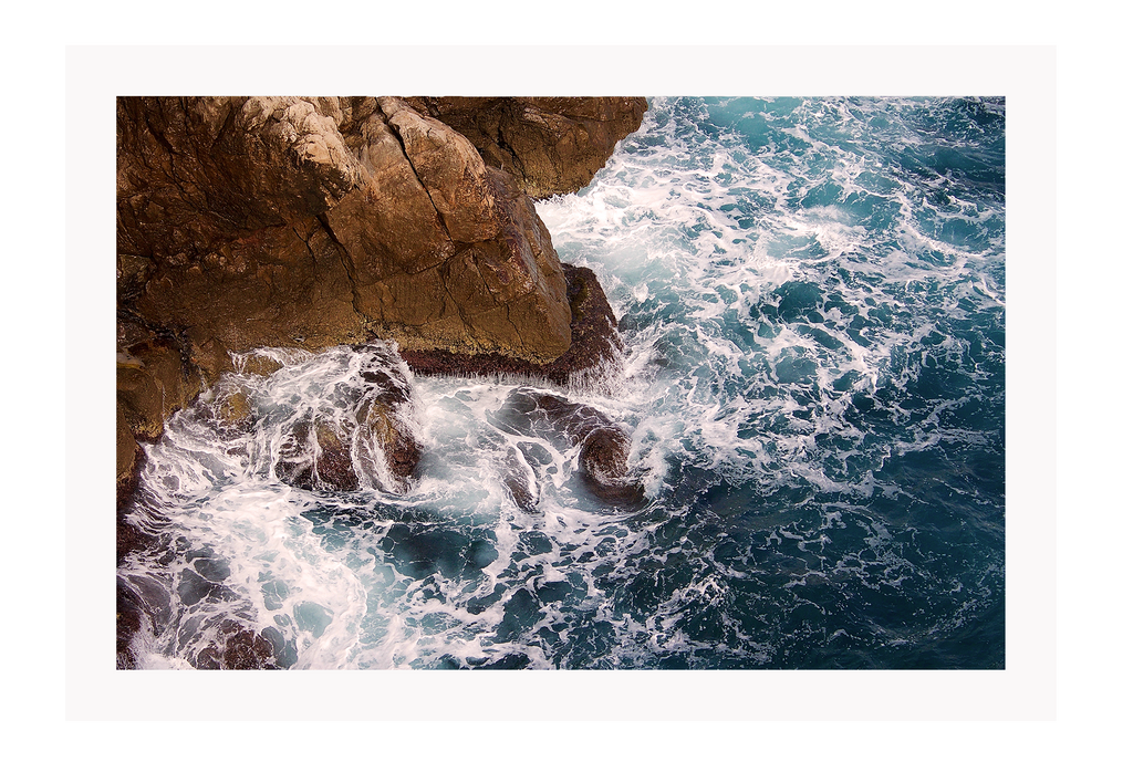 A natural wall art with a blue ocean rocks crashing waves on coastline white wash.