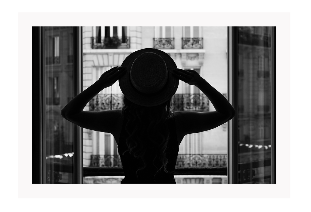 A vintage fashion wall art with a cinematic scene of a parisian woman wearing a hat looking out to the city on the balcony. 