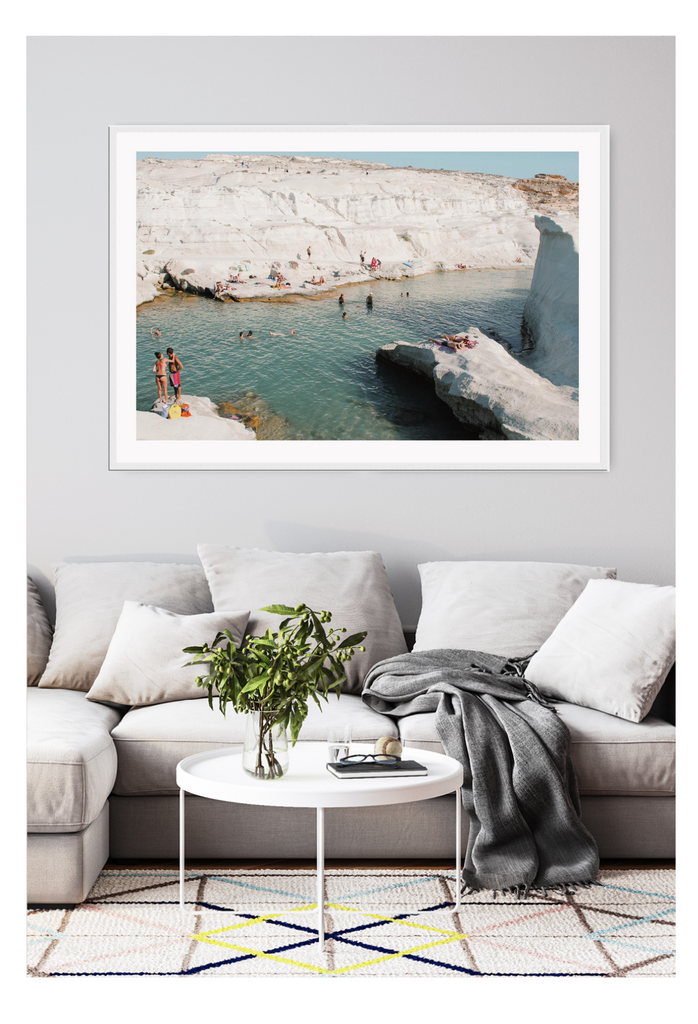 Coastal style photography beach landscape print with white rocks surrounding a reef and people swimming and sunbathing.