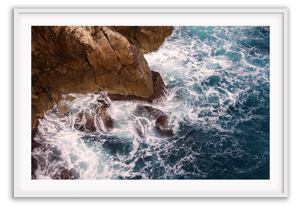 A natural wall art with a blue ocean rocks crashing waves on coastline white wash.