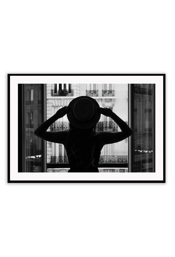 A vintage fashion wall art with a cinematic scene of a parisian woman wearing a hat looking out to the city on the balcony. 