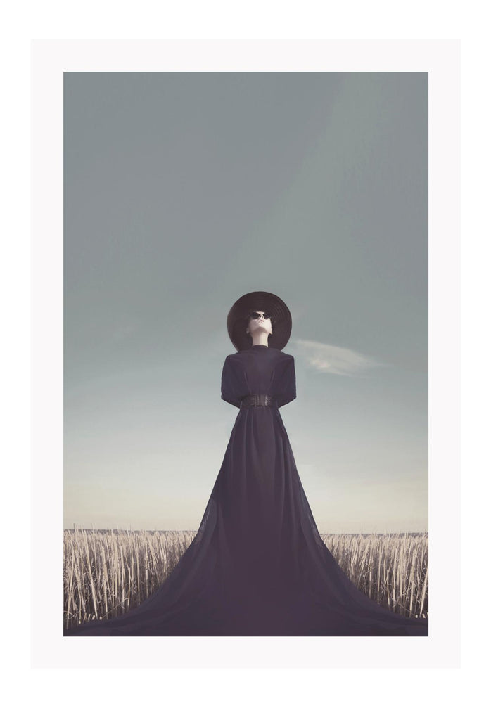 Photography print with woman in black dress and hat looking at sky in field washed natural colours