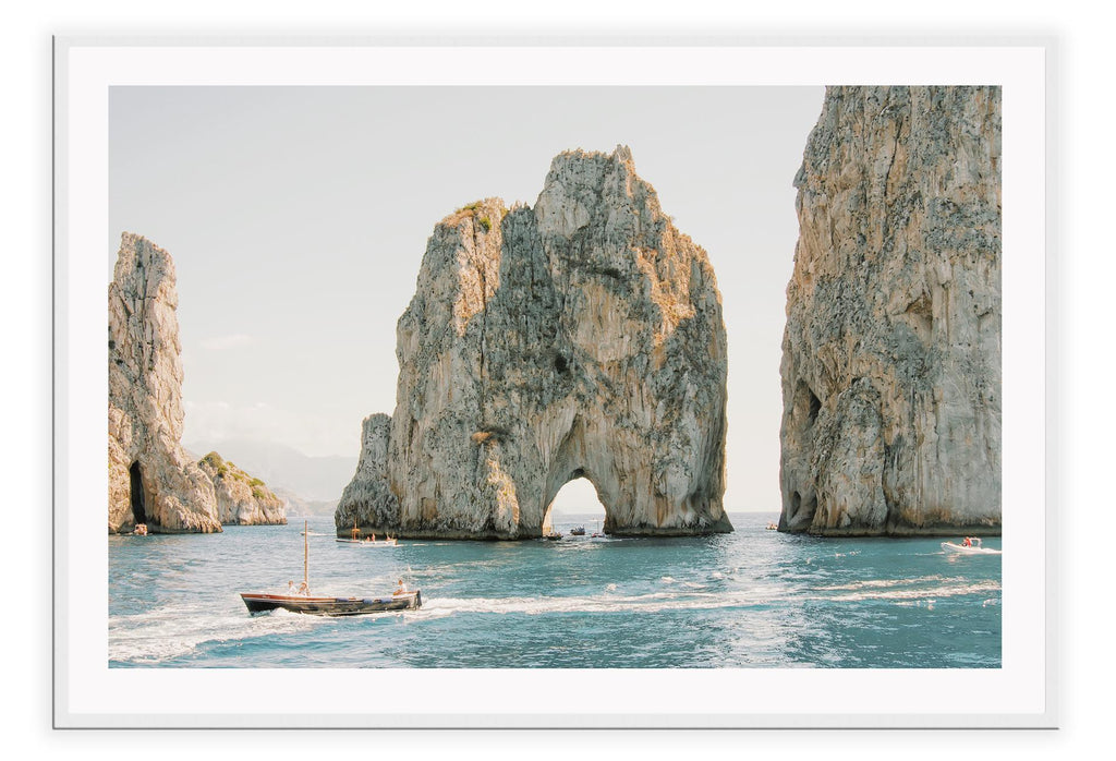 Coastal style photography beach landscape print with large grey rocks and a boat in the ocean.